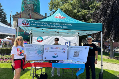 Picture of members of the Equity, Diversity, Inclusion and Belonging Committee standing under a tent outside at Museum Square in Woodstock for the Oxford Pride Event.